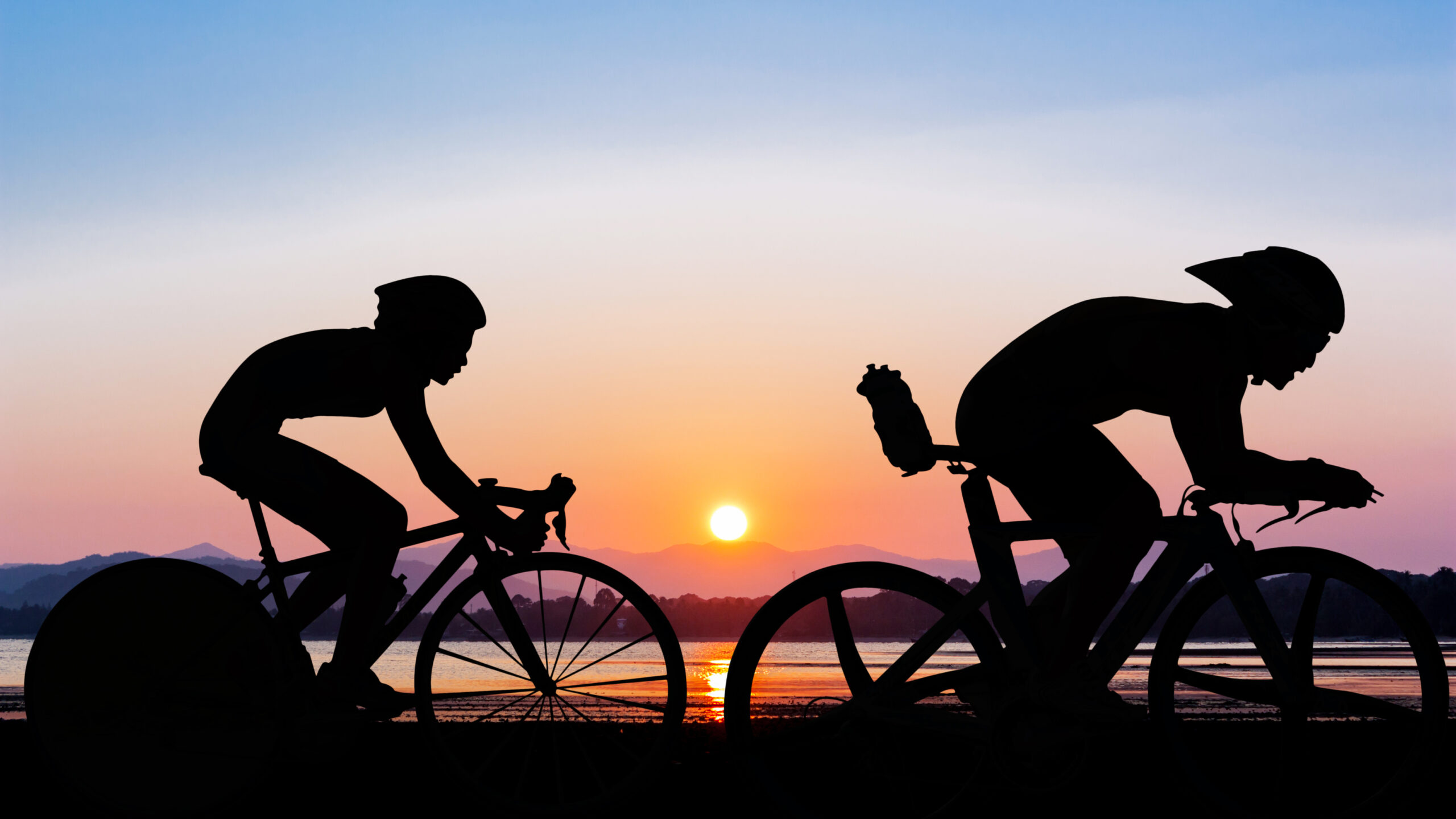 Two cyclists silhouetted against a vibrant sunset.
