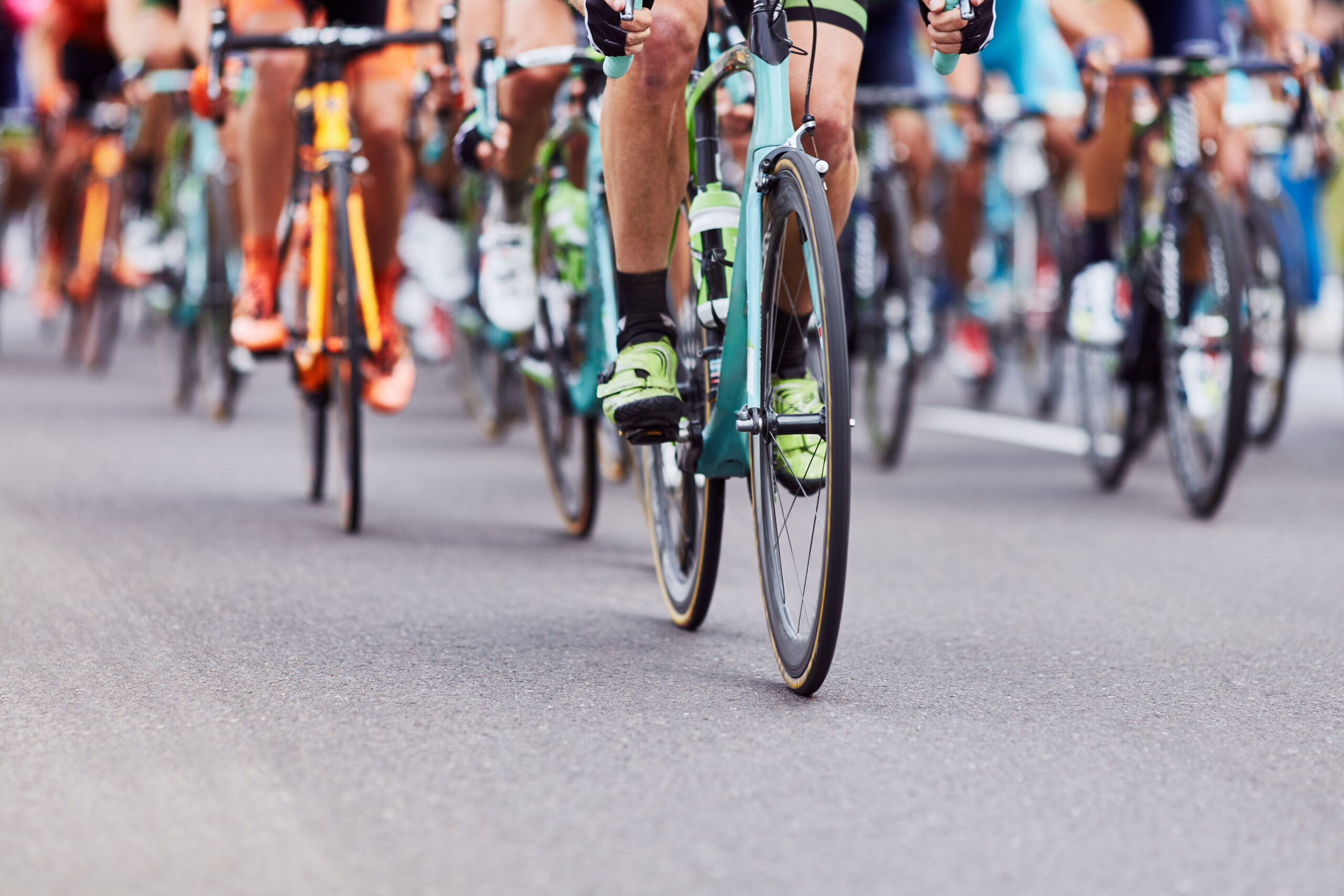 Cyclists race on a road with a close-up of front wheels and legs.